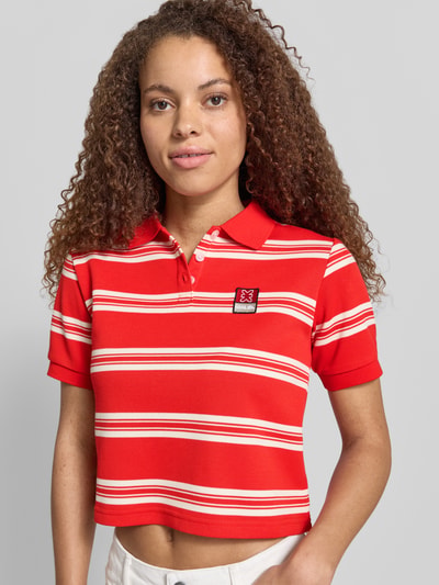 Frauenmodel trägt Cropped Poloshirt mit Label-Patch von Karo Kauer in Rot mit Streifen, Material-Mix, Straight Fit, Polokragen, kurze Knopfleiste, Rückenlänge bei Größe S: 47 cm, Ganzkörperansicht von vorne.