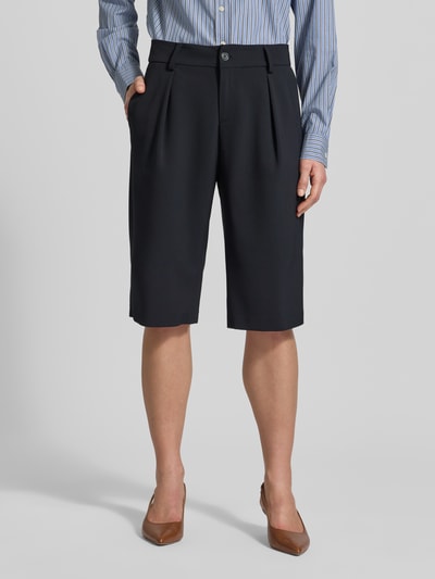 Kobiece modelka nosi czarne bermudy Loose Fit Bermudas mit Knopfverschluss Modell 'MILLA' od BRAX, mieszanka materiałów z dodatkiem żywej wełny, szerokość w rozmiarze 36: 41 cm, długość wewnętrzna nogawki: 36 cm, boczne i tylne kieszenie, zapinane na guzik i zamek błyskawiczny, widok całej sylwetki z przodu.