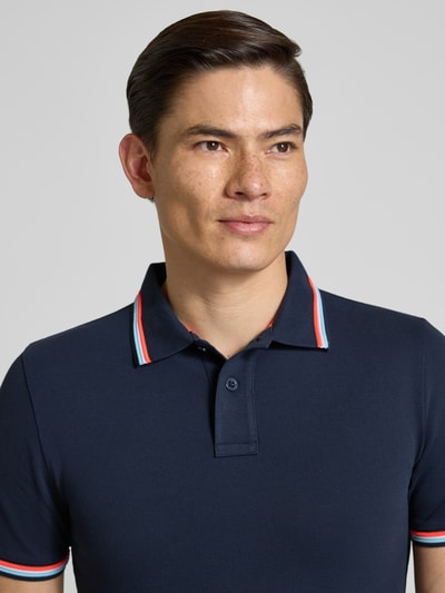 Męski model nosi koszulkę polo Slim Fit Poloshirt mit Kontraststreifen Modell 'Brice' von Sundek z mieszanki bawełny i elastanu, kolor granatowy, paski w kontrastowym kolorze, listwa guzikowa, długość tyłu w rozmiarze M: 70 cm, zbliżenie na górną część tułowia z przodu.