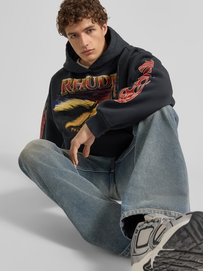 Männermodel trägt Hoodie mit Kapuze von RHUDE in Schwarz mit Label-Print und Känguru-Tasche, Reine Baumwolle, Lockerer-Schnitt, Nahaufnahme Oberkörper.