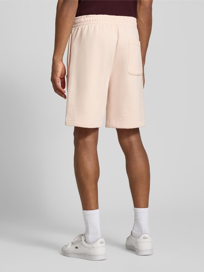 Männermodel trägt Regular Fit Shorts aus Baumwoll-Mix von Lacoste in Hellbeige, lockere Passform, glatte Struktur, Ganzkörperansicht Rückansicht. Herren Sweatshorts von Lacoste.