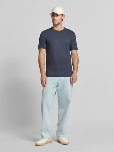 Męski model trägt Regular Fit T-Shirt aus Baumwoll-Mix Modell 'Tegood' von BOSS Orange w kolorze granatowym, jasnoniebieskie jeansy, białe sneakersy, jasna czapka, jednorodne tło, Ganzkörperansicht von vorne.