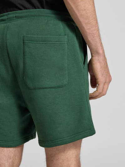 Mężczyzna nosi Regular Fit Shorts aus Baumwoll-Mix von Tommy Jeans, efekt: jednolity kolor, detal z logo, dzianina dresowa, kieszeń z tyłu, krój regular fit, tunel, elastyczny ściągacz, wpuszczane kieszenie, mieszanka bawełny, szorstka tekstura, zdjęcie z tyłu, zbliżenie na dolną część ciała.