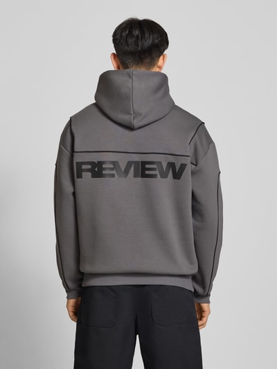 Männermodel trägt Hoodie mit Logo und Känguru-Tasche von REVIEW in Grau, Baumwoll-Mix, Regular-Fit, Rückenlänge 71 cm, Ganzkörperansicht Rückansicht.