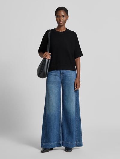 Frauenmodel trägt Relaxed Fit Pullover aus Viskose-Mix Modell 'Thamira' von MSCH Copenhagen, Strick-Optik, dunkel, mit 1/2-Arm und Rundhalsausschnitt, kombiniert zu weiter Jeans, Ganzkörperansicht von vorne.
