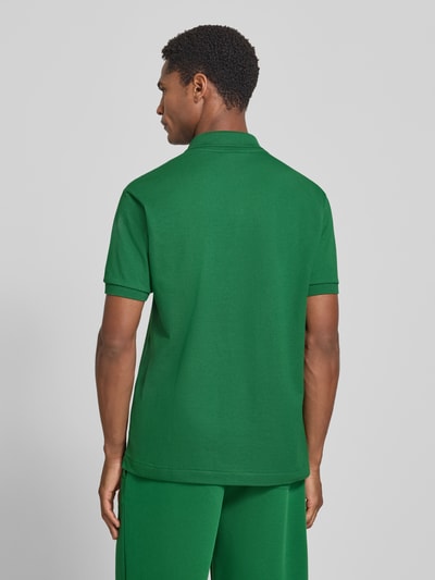 Männermodel trägt Regular Fit Poloshirt aus reiner bawełna model 'CORE' od Lacoste, kolor zielony, tekstura gładka, Ganzkörperansicht Rückansicht. Koszulka polo męska od Lacoste.