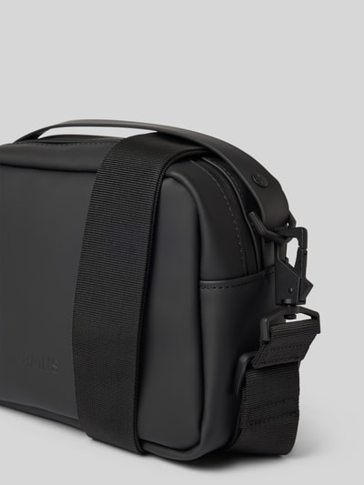 Produktfoto, Box Bag mit Logo-Detail von Rains in mattem Schwarz, robuste eckige Form, sichtbarer Reißverschluss, glatte Textur, abnehmbarer breiter Trageriemen, Hauptfach mit Steckfach innen, Kompaktmaß 21x17x8 cm, Schulterriemen 82 cm