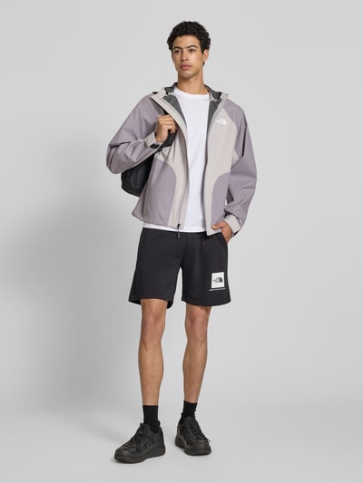 Männermodel trägt Regenjacke mit Logo von The North Face in Grau mit Kapuze und Reißverschluss, Regular-Fit, Ganzkörperansicht von vorne, Rückenlänge bei Größe M: 70 cm, Schulterbreite: 50 cm, Brustweite: 62 cm, Ärmellänge: 76 cm.