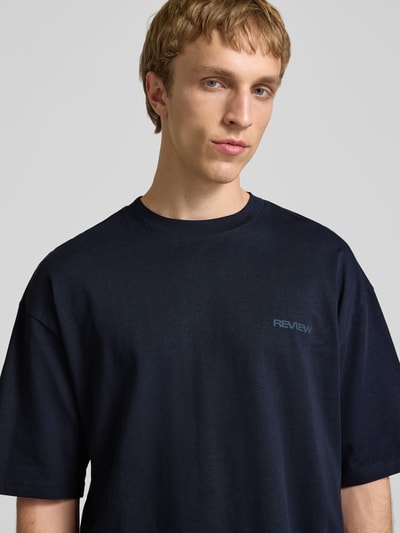 Männermodel trägt Oversized T-Shirt mit Logo von REVIEW in Dunkelblau aus reiner Baumwolle, Rundhalsausschnitt, Nahaufnahme Oberkörper.