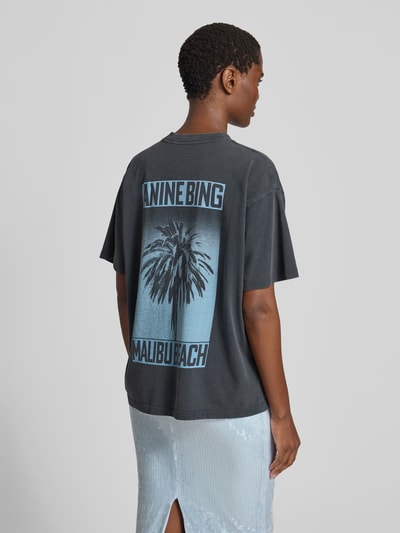 Frauenmodel trägt Oversized Fit T-Shirt mit Logo-Print von Anine Bing aus reiner Baumwolle in Schwarz mit blauem Print, Ganzkörperansicht Rückansicht.