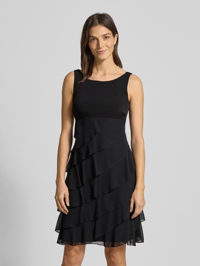 Frauenmodel trägt Knielanges Cocktailkleid mit Volants von Swing aus schwarzem Chiffon in A-Linie, Rundhalsausschnitt, Ganzkörperansicht von vorne. Rückenlänge bei Größe 36: 103 cm, Brustweite: 31 cm.