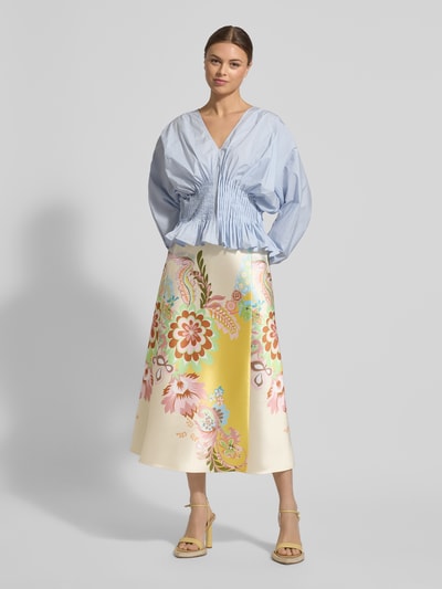 Modelka nosi Spódnica midi aus Satin im Allover-Look von HERZENS w linii A, wzór na całej powierzchni, szwy działowe, szerokość w rozmiarze 36: 36 cm, całkowita długość: 87 cm, jasne kolory i kwiatowe motywy, gładka satynowa powierzchnia. Ganzkörperansicht von vorne.