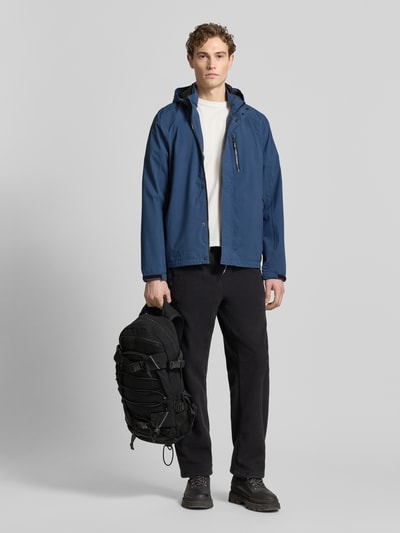 Männermodel trägt Jacke mit Napoleontasche Modell 'KOS' von Killtec in Blau, Gerade Passform, Kapuze mit Tunnelzug, Ganzkörperansicht von vorne. Rückenlänge bei Größe M: 73 cm, Schulterbreite 46 cm, Brustweite 60 cm, Ärmellänge 71 cm, durchgehender Reißverschluss mit Abdeckleiste, Ärmelriegel, Label-Patch.