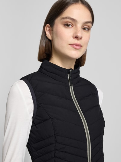 Kobiece modelka nosi Steppweste mit 10.000 mm Wassersäule Modell 'GS109' von G.I.G.A. DX, czarna, krój slim fit, stójka, zamek, kieszenie na zamek, długość pleców w rozmiarze 36: 61 cm, szerokość ramion w rozmiarze 36: 37 cm, szerokość klatki piersiowej w rozmiarze 36: 49 cm, prosta tekstura, widok z przodu, zbliżenie górnej części ciała.