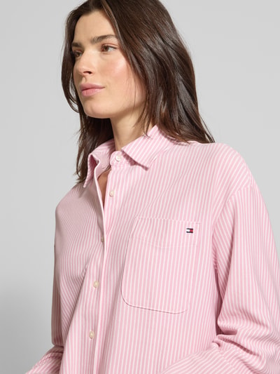 Frauenmodel trägt Oversized Langarmbluse aus Baumwoll-Mix von Tommy Hilfiger, rosa mit weißen Streifen, Brusttasche, Nahaufnahme Oberkörper.