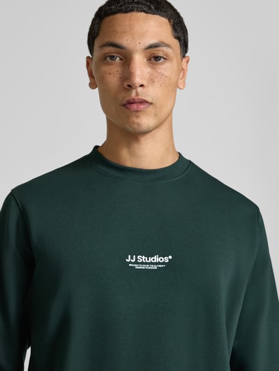Männermodel trägt Regular Fit Sweatshirt aus Baumwoll-Mix Modell 'Soho' von JACK & JONES in Dunkelgrün mit Logo-Print, Nahaufnahme Oberkörper.
