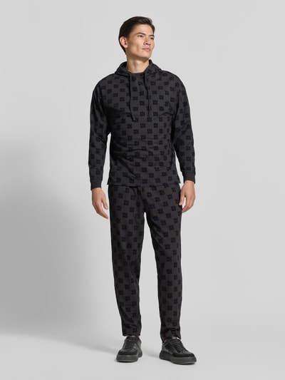 Männermodel trägt Regular Fit Sweathose aus Baumwoll-Mix von HUGO in Dunkelgrau mit Allover-Logo-Muster, Ganzkörperansicht von vorne. Herren Sweathose von HUGO