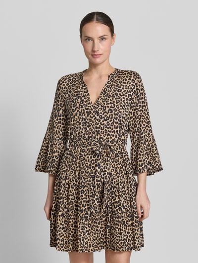 Vrouwenmodel draagt tailliertes Tunikakleid aus reiner Viskose Modell 'MELBA' van Vero Moda met all-over patroon, v-hals, trompetmouwen, volantzoom en bindriem, mini lengte, getailleerde fit, detailopname bovenlichaam, voorkant.