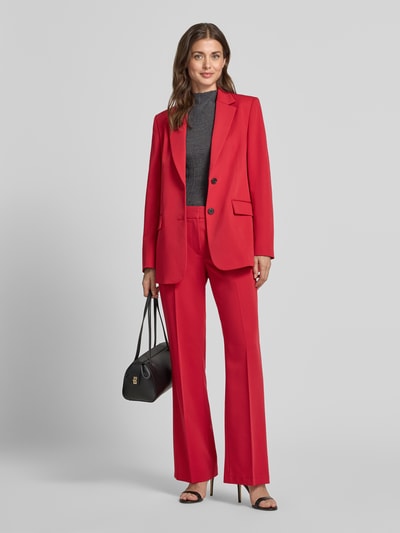 Vrouwenmodel draagt Regular Fit Longline Blazer met klepzakken van JAKE*S WOMAN collectie in felrood met sierknopen, deelnaden, knopen, kraag, schoudervullingen, loopsplit, 2-knoopsluiting, lange mouw en rechte vormen, klepzak als detail, geheel gladde textuur, full body vooraanzicht.