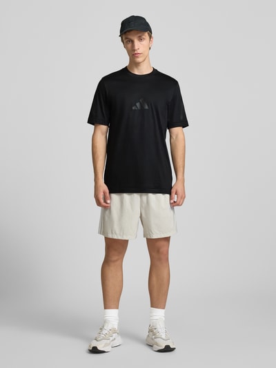 Męski model nosi Regular Fit T-Shirt aus reiner Baumwolle von adidas Sportswear, efekt: jednolity kolor, krój regular fit, nadruk z logo, okrągły dekolt, krótki rękaw, bawełna, Ganzkörperansicht von vorne.