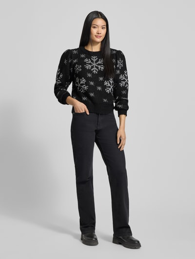 Frauenmodel trägt Regular Fit Weihnachtspullover mit Allover-Muster Modell 'NEWSNOWFROST' von Vero Moda in Schwarz mit weißen Schneeflocken, Motiv-Print, Rundhals, Langarm, gerippter Rumpfabschluss, Strick; Ganzkörperansicht von vorne.