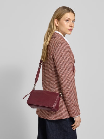 Frauenmodel trägt Handtasche mit Label-Detail Modell 'CLARICE' von LIEBESKIND BERLIN in Dunkelrot, Reißverschluss, Schulterriemen, Ganzkörperansicht Rückansicht.