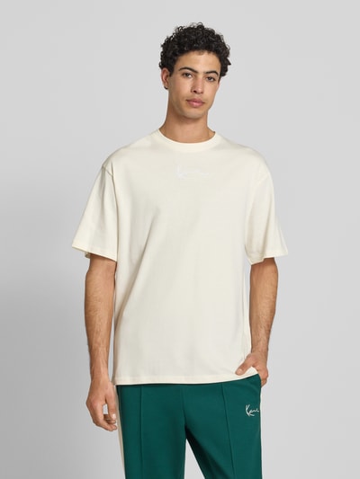 Männermodel trägt T-Shirt mit Label-Stitching und Rundhalsausschnitt von KARL KANI, Herren T-Shirt aus Reine Baumwolle, Relaxed-Fit, Frontansicht, Rückenlänge bei Größe M 70 cm.