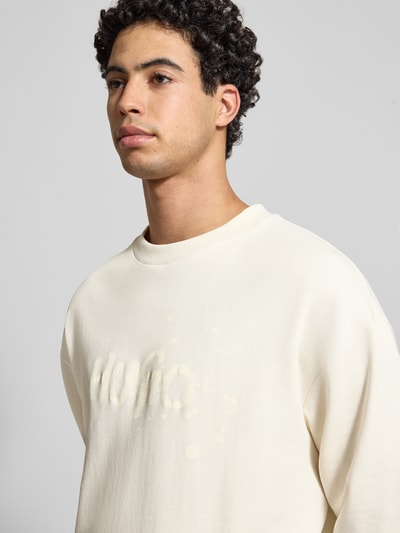 Männermodel draagt Regular Fit Sweatshirt aus reiner Baumwolle Modell 'NIEROFIX_CREW' van Hugo Blue in effen crème met labelprint, geribde randen, rondhals, sweatmateriaal, Nahaufnahme Oberkörper.