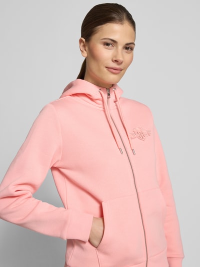 Vrouwenmodel draagt Sweatjacke mit Zweiwege-Reißverschluss und Label-Stitching van Gant in lichtroze katoenmix, regular fit, capuchon met trekkoord, kangoeroezak, detailopname bovenlichaam.