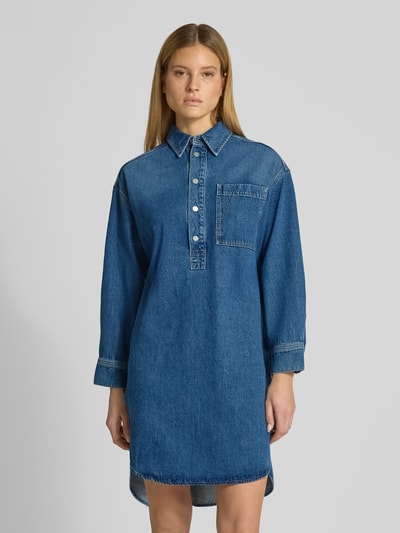 Vrouwenmodel draagt Oversized Jeanskleid aus Lyocell-Mix van Armedangels in denimlook, oversized fit, midilengte, ronde hals, labelpatch, strikceintuur, korte knoopsluiting, lange mouw met manchet, rechte zoom en borstzak, materiaal lyocellmix. Ganzkörperansicht van voren.