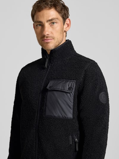 Männermodel trägt schwarze Regular Fit Jacke mit Stehkragen Modell 'Peter' von Didriksons, Strukturmuster, Nahaufnahme Oberkörper.