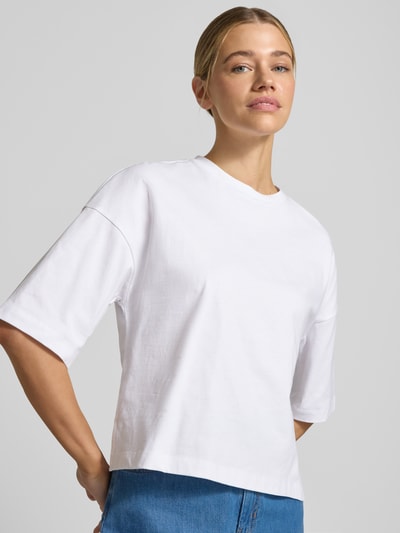 Modelka kobieca ma na sobie T-Shirt z obniżoną linią ramion model 'Sarenzi' od OPUS, czysta bawełna, krój loose fit, dekolt okrągły, kolor biały, długość pleców w rozmiarze S: 52 cm, zbliżenie na górną część ciała, widok z przodu.