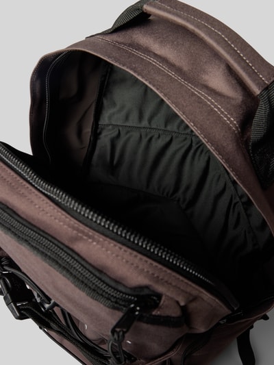 Productfoto, Rucksack mit Label-Details Modell 'KICKFLIP' van Carhartt Work In Progress in bruin en zwart met ritssluiting, verstelbare schouderriem, korte draaghengsel, binnen- en buitenvakken, kliksluitingen, breedte 36 cm, lengte 48 cm, diepte 18 cm, schouderriemlengte 63 cm, detailopname.