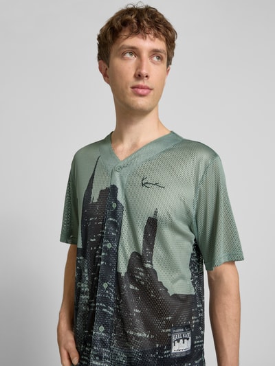 Męski model nosi Modern Fit Freizeithemd mit V-Ausschnitt od KARL KANI z siateczki, grafika, logo, długość pleców 68 cm, szerokość w rozmiarze M 50 cm, długość rękawa 27 cm, krój modern fit, widok na górną część ciała z przodu