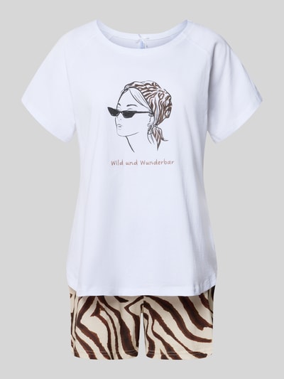 Frauenmodel trägt Pyjama mit Motiv und Stitching Modell 'Wild und Wunderbar Short' von LOUIS & LOUISA aus reiner Baumwolle, Relaxed-Fit, weißes Pyjama-Oberteil mit Motiv und Schriftzug, gemusterte Shorts in Braun und Beige, Ganzkörperansicht von vorne.