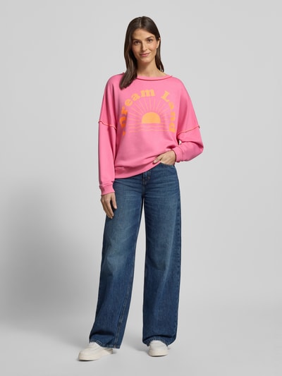 Frauenmodel trägt Oversized Sweatshirt mit gerippten Abschlüssen von miss goodlife in Pink mit gelbem Statement-Print, Ganzkörperansicht von vorne.