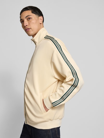 Männermodel trägt Relaxed Fit Sweatjacke mit Kontraststreifen Modell 'RIBER' von Only & Sons in Optik: Unifarben, Materialverarbeitung: Sweat, Farbe Beige mit grünen Streifen, seitliche Eingrifftaschen, Stehkragen, Langarm, Reißverschluss, Ganzkörperansicht Rückansicht.