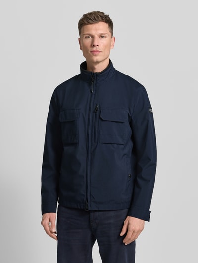 Männermodel trägt Jacke mit Stehkragen von NAUTGÅRD in Dunkelblau mit Reißverschluss, Eingrifftaschen, Brusttaschen, Regular Fit, Ganzkörperansicht von vorne. Rückenlänge bei Größe M: 73 cm, Schulterbreite: 45 cm, Brustweite: 49 cm, Ärmellänge: 67 cm.
