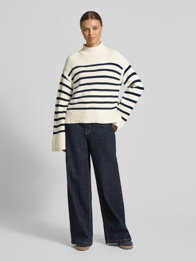Frauenmodel trägt Regular Fit Pullover aus Woll-Mix Modell 'Sharad' von Lauren Ralph Lauren, cremefarben mit dunkelblauen Streifen, Stehkragen, breite Abschlüsse, Materialmix mit Baumwolle, Ganzkörperansicht von vorne.