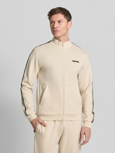 Männermodel trägt Sweatjacke mit Stehkragen und Zweiwege-Reißverschluss von EA7 Emporio Armani in Beige mit Label-Detail, Eingrifftaschen, Regular-Fit; Ganzkörperansicht von vorne. Rückenlänge bei Größe M: 68 cm, Ärmellänge 67 cm.