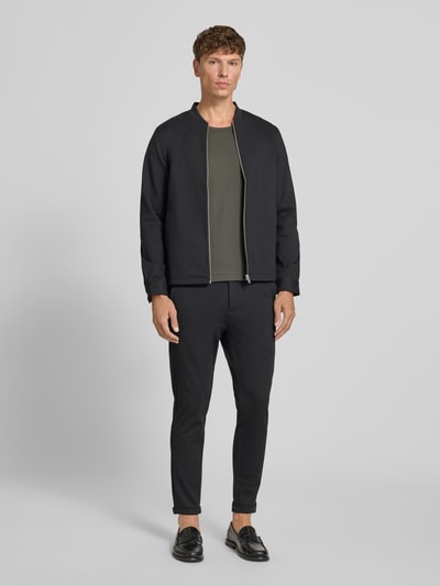 Męskimodel nosi Regular Fit Sweatjacke mit Stehkragen od Lindbergh, elastyczna mieszanka materiałów, zamek błyskawiczny, wpuszczane kieszenie, kolor czarny, długość tyłu w rozmiarze M: 69 cm, długość rękawów w rozmiarze M: 66 cm, krój regular fit, Ganzkörperansicht von vorne.