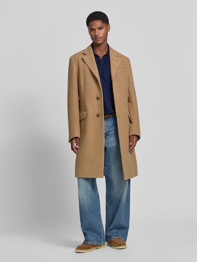Männermodel trägt Slim Fit Poloshirt aus reiner Baumwolle von Polo Ralph Lauren in Dunkelblau, dazu beiger Mantel und Jeans, Ganzkörperansicht von vorne.