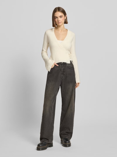 Kobiece modelka nosi Kardigan in Wickel-Optik od Gina Tricot, mieszanka materiałów z domieszką wełny z alpaki, krój slim fit, kopertowy styl, dekolt w serek, długość tyłu 47 cm, długość rękawa 66 cm, widok cała sylwetka z przodu.