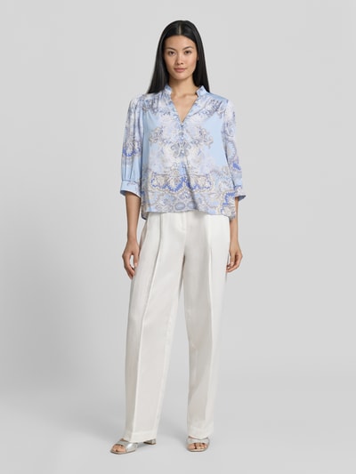 Frauenmodel trägt Regular-Fit Damen Bluse mit 3/4-Arm Modell 'Roselle Artist Paisley' von Neo Noir in Hellblau mit Allover-Look, Stehkragen, V-Ausschnitt und Knopfleiste, seidig glänzende Textur, Ganzkörperansicht von vorne. Rückenlänge bei Größe 36: 57 cm, Ärmellänge: 43 cm.