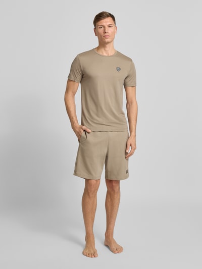 Männermodel trägt T-Shirt aus Viskose-Mix mit Label-Patch von EA7 Emporio Armani in Beige, Slim-Fit, Ganzkörperansicht von vorne.