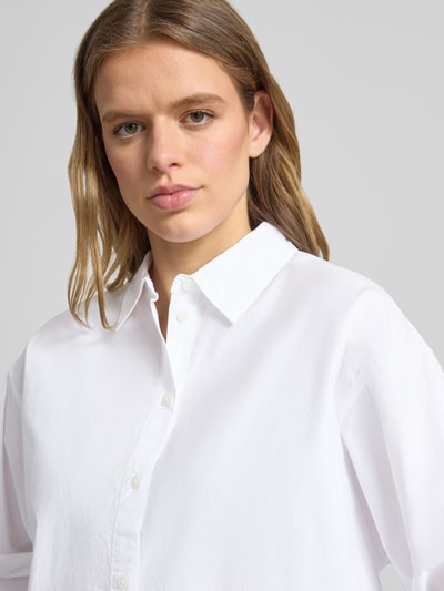 Kobiece model prezentuje Basic Hemd aus Baumwolle mit Hemdblusenkragen od Review, biała bawełna, krój regular fit, listwa guzikowa, sportowe mankiety, zaokrąglony dół, długość tyłu w rozmiarze S: 73 cm, długość rękawów w rozmiarze S: 55 cm, zbliżenie na górną część ciała