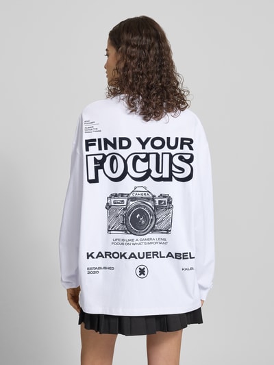 Frauenmodel trägt Oversized Longsleeve mit Statement-Print von Karo Kauer, weiße Baumwolle, schwarze Akzente, Ganzkörperansicht Rückansicht.
