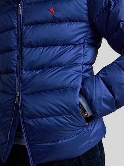 Mężczyzna nosi kurtkę pikowaną Regular Fit Steppjacke mit Logo-Stitching von Polo Ralph Lauren, jednokolorowy, krój regular fit, zamek błyskawiczny, aplikacja z wyhaftowanym logo, rękaw długi, boczne wpuszczane kieszenie, stójka, zdjęcie: zbliżenie na górną część ciała.