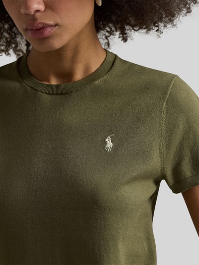 Modelka nosi Regular Fit Kurzarmpullover mit Logo-Stitching von Polo Ralph Lauren, mieszanka bawełny, okrągły dekolt, wyhaftowane logo, elastyczne zakończenia rękawów, oliwkowy kolor, gładka tekstura, zbliżenie na górną część ciała