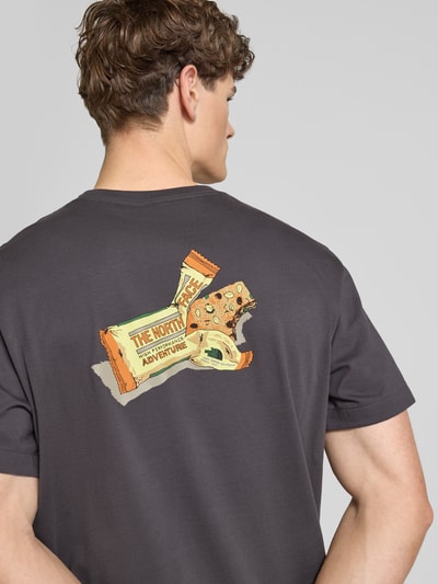 Mannenmodel draagt Relaxed Fit T-Shirt uit pure katoen van The North Face in antraciet met kleurrijke labelprint op de rug, rond hals, rechte zoom, relaxed fit, ruglengte maat M 72 cm. Ganzkörperansicht Rückansicht.